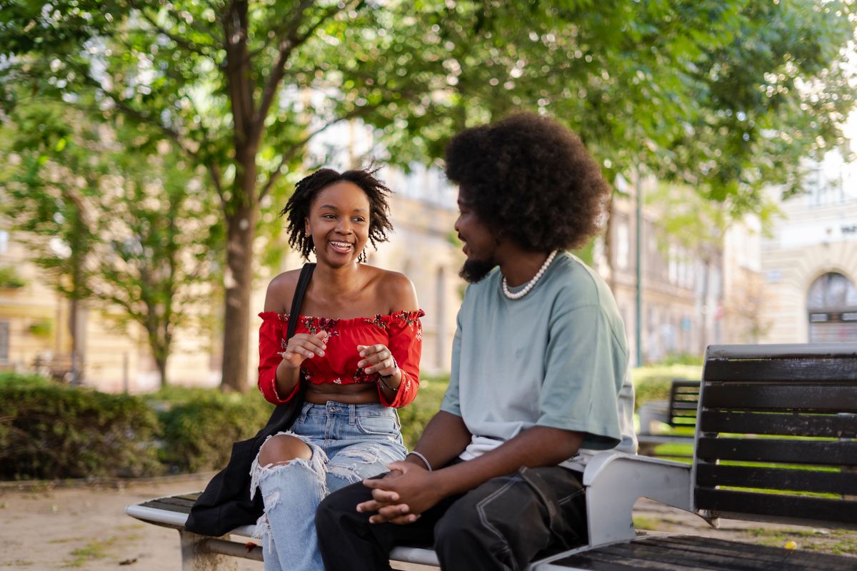 Un couple souriant discute sur un banc dans un parc