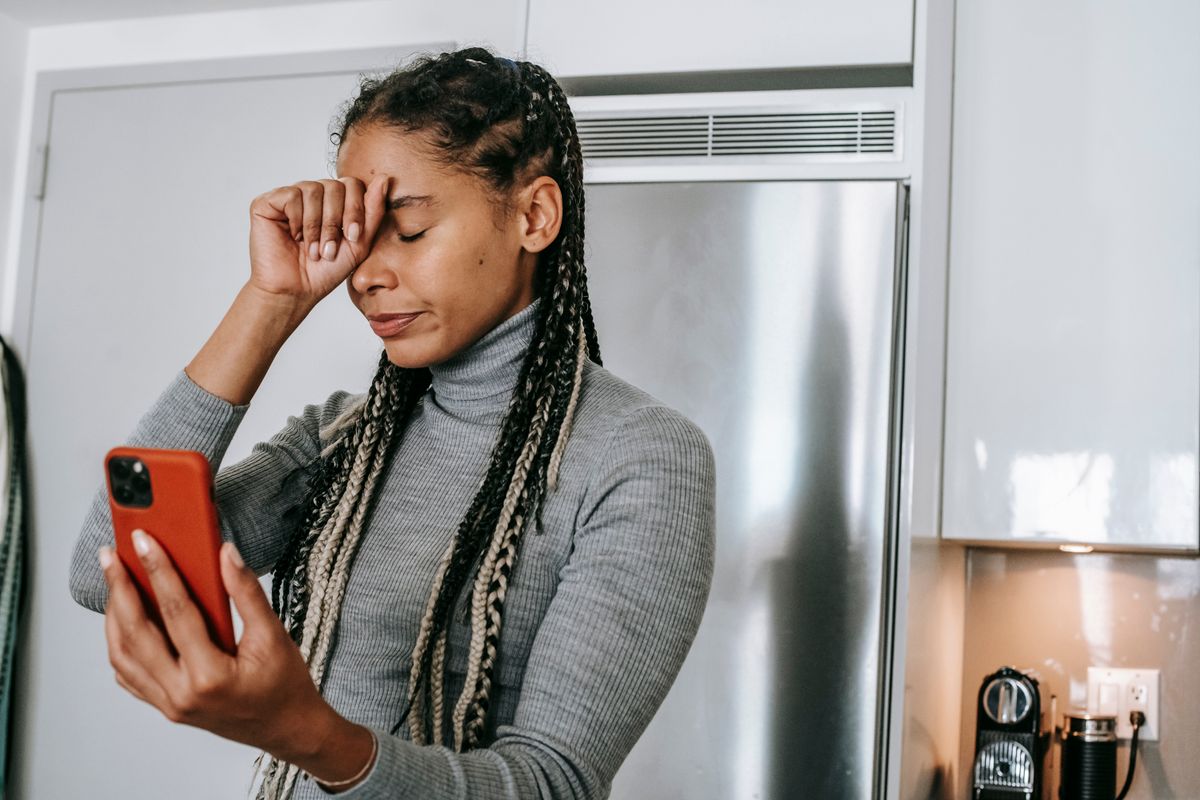 Une jeune femme regarde son téléphone, la main sur le front, l’air soucieux